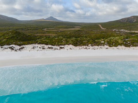 Aerial view of Hellfire Bay featuring pristine white sand, turquoise ocean waves, and coastal scrubland in Cape Le Grand National Park, Western Australia, Australia.
