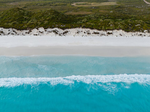 Aerial view of Hellfire Bay featuring turquoise waves crashing onto white sand beaches with lush green coastal vegetation in Cape Le Grand National Park, Western Australia, Australia.