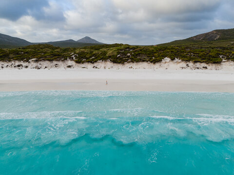Aerial view of Hellfire Bay with turquoise waves washing onto white sand and a person walking along the shore in Cape Le Grand National Park, Western Australia, Australia.