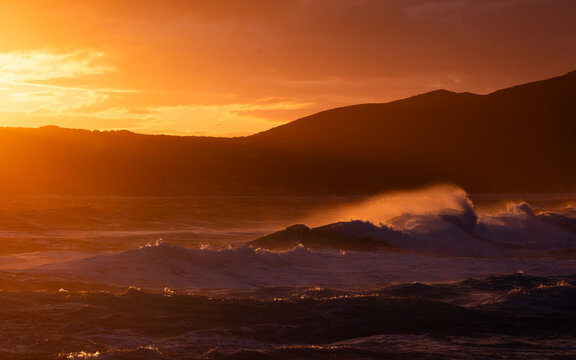 View of the sunset over the ocean with crashing waves and the silhouette of the coastline near Blowholes Road in Torndirrup, Western Australia, Australia.