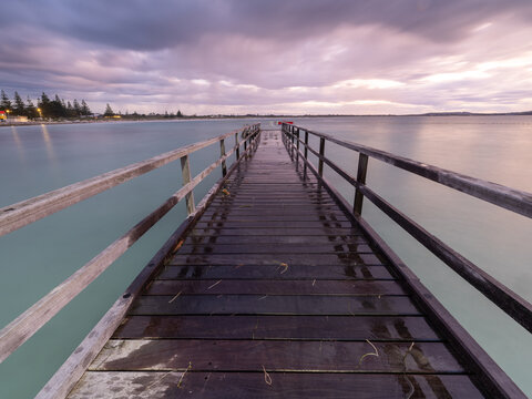 View of the wooden jetty extending into the calm water under a cloudy twilight sky in Emu Point, Western Australia, Australia.