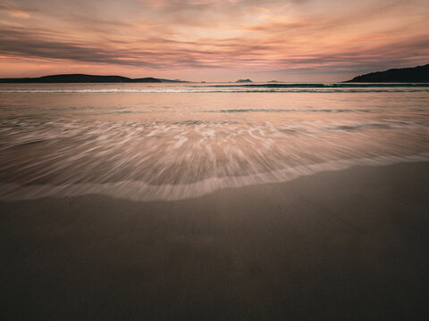 View of Middleton Beach at sunset with gentle waves washing over the wet sand under a soft pink and orange sky, Middleton Beach, Western Australia, Australia.