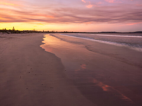 View of Middleton Beach at sunset with calm waves washing onto the sandy shore under a vibrant pink and orange sky in Middleton Beach, Western Australia, Australia.