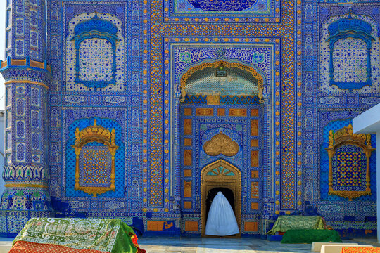 View of the Shrine of Sachal Sarmast featuring intricate blue and gold tile work and a person in a white garment standing at the entrance in Daraza Sharif, Sindh, Pakistan.
