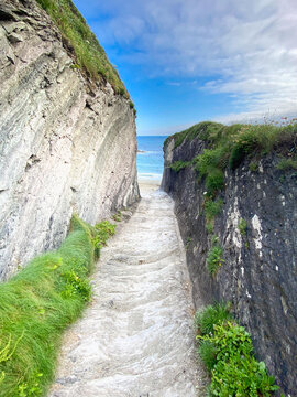 View of the narrow, steep stone path leading down through dramatic rock cliffs to the sandy shore of Lansallos Beach in Looe, Cornwall, United Kingdom.