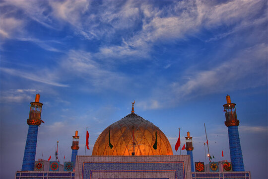 View of the golden dome and minarets of the Sehwan Sharif shrine decorated with colorful flags under a blue sky in Sehwan, Sindh, Pakistan.