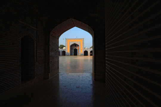 View of the courtyard of the historic Shah Jahan Masjid, framed by a dark arched doorway, showcasing intricate blue tile work and architectural details in Thatta, Sindh, Pakistan.