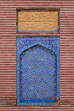 View of the intricate blue and white geometric tile work and Arabic calligraphy inscription on the red brick wall of the historic Shah Jahan Masjid in Thatta, Sindh, Pakistan.