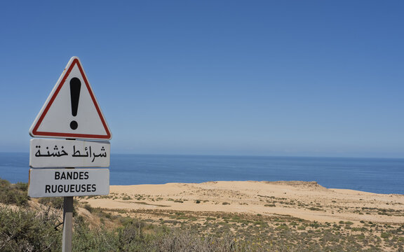 View of a road sign warning of rough strips overlooking the sandy coastline and the Atlantic Ocean in Tamri, Souss-Massa, Morocco.