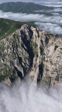 Vertical 4K UHD Drone Flight Over Massive Rocky Cliffs Rising Through a Sea of Clouds.