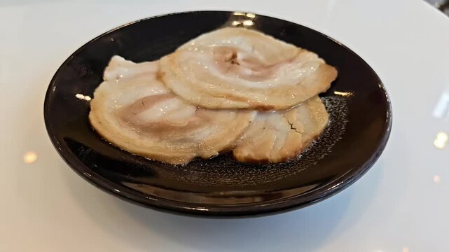 Roasted chashu pork belly roll slices on a plate, Ramen Topping, Japanese Food Cuisine, Meat Roast, Slow Motion Rotating Shot