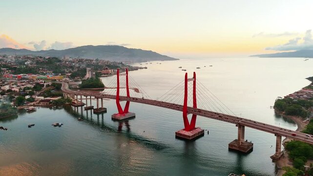Aerial view of Jembatan Merah Putih bridge spanning the bay with red towers at sunset in Kecamatan Sirimau, Maluku, Indonesia.