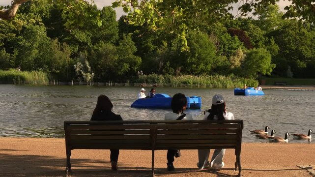 People on a bench watching pedal boats on a park lake