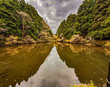 View of Lake Ashinoko surrounded by dense cedar forests with calm water reflecting the cloudy sky in Hakone, Kanagawa, Japan.