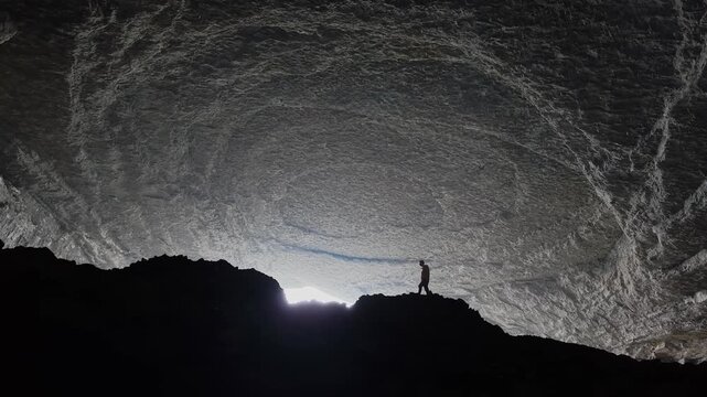 Aerial view of a person standing on a rocky ledge inside the massive Zhijin Shexiang Cave also called Musk Cave with rock formations and a natural light opening in Bijie, Guizhou, China.