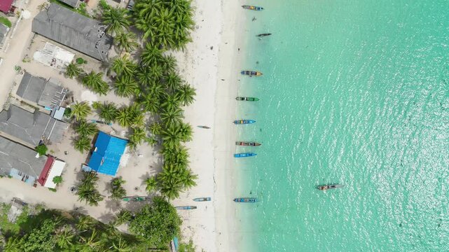Aerial view of Pantai Ohoidertutu Ngur Mun Vat Wahan with turquoise water, white sand, palm trees, and small boats along the coast in Kei Kecil Barat, Maluku, Indonesia.