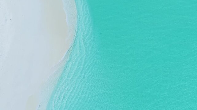 Aerial view of white sand beach meeting the clear turquoise ocean water in Vashafaru, Haa Alif Atoll, Maldives.
