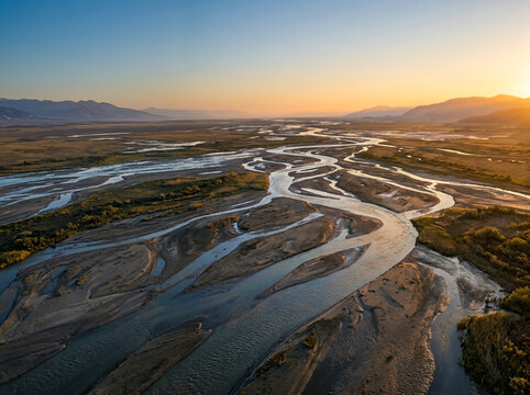 Aerial view of a braided river through a grassy valley at golden sunset