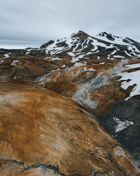 Aerial view of Kerlingarfjoll mountain range with geothermal steam rising from orange rhyolite slopes and patches of snow in Hrunamannahreppur, Iceland.