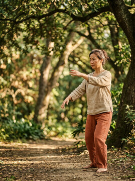 Woman practising tai chi outdoors in a wooded area in loose earthy clothing