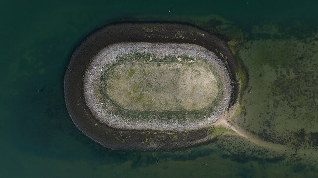 Aerial view of the Schelphoek, an oval-shaped island with a rocky perimeter and grassy center surrounded by calm water in Serooskerke Schouwen, Zeeland, Netherlands.