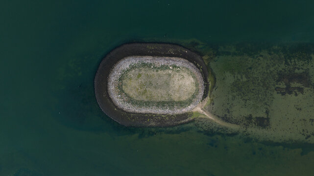 Aerial view of the Schelphoek island with its oval shape, grassy center, and stone perimeter surrounded by calm water in Serooskerke Schouwen, Zeeland, Netherlands.