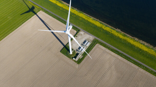 Aerial view of a single wind turbine standing in a cultivated field near a road and a body of water in Ooltgensplaat, South Holland, Netherlands.