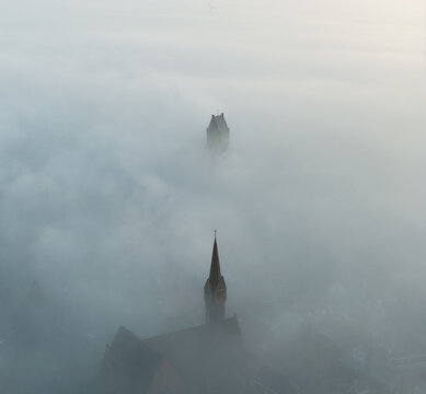 Aerial view of church towers rising above a thick layer of morning fog in Bolsward, Friesland, Netherlands.