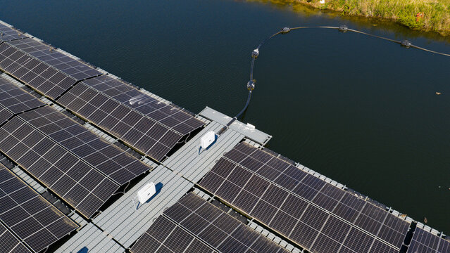 Aerial view of a floating solar farm with rows of photovoltaic panels on a water surface, connected by a central walkway and a floating cable in Zwolle, Overijssel, Netherlands.