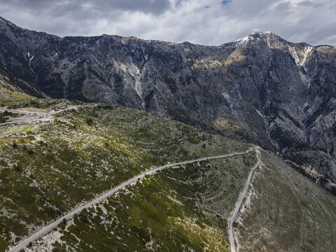 Aerial view of Llogara Pass with winding mountain roads cutting through rugged terrain and steep slopes in Himare, Vlore County, Albania.
