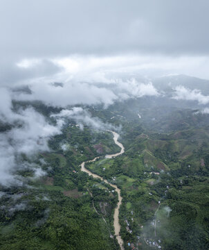 Aerial view of the lush green mountains and the winding river of Semuc Champey, partially obscured by low-hanging clouds in San Agustin Lanquin, Alta Verapaz, Guatemala.