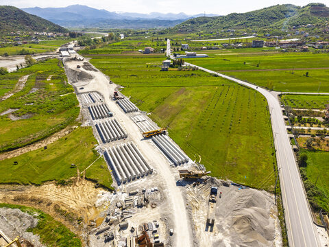 Aerial view of the construction site for a new road featuring rows of concrete beams and heavy machinery amidst green agricultural fields in Paper, Elbasan County, Albania.
