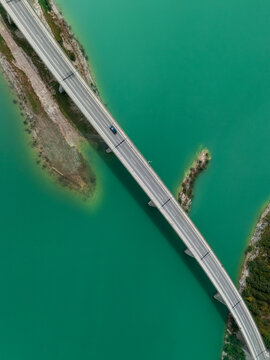 Aerial view of the Sylvenstein bridge crossing over vibrant turquoise water with small islands and lush green banks in Bavaria, Germany.