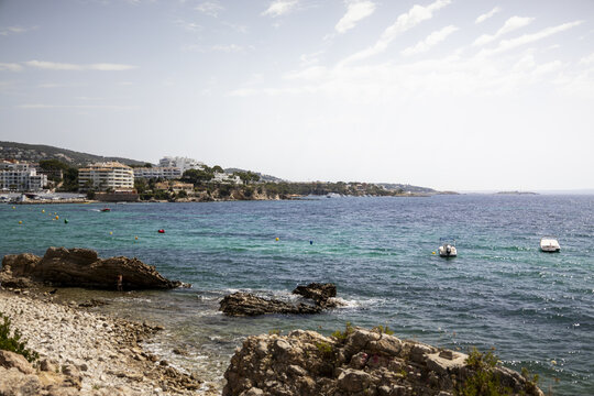 View of the turquoise Mediterranean Sea at Palma Nova, with rocky shoreline, small boats, and coastal buildings in Palma Nova, Balearic Islands, Spain.