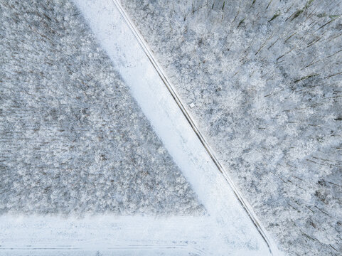Aerial view of a snow-covered forest landscape with a narrow path cutting through the trees in Hesse, Germany.