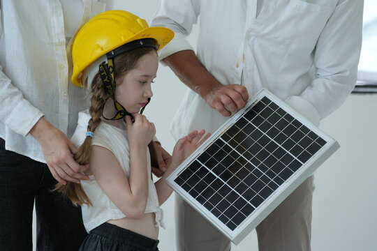 Young parents teaching their curious child let the girl in a toy helmet touch the photovoltaic cells up close in their future eco friendly house in warm natural light