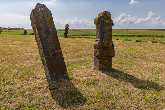 View of Strieperkerkhof with weathered historic gravestones standing in a grassy field under a blue sky in Baaiduinen, Friesland, Netherlands.
