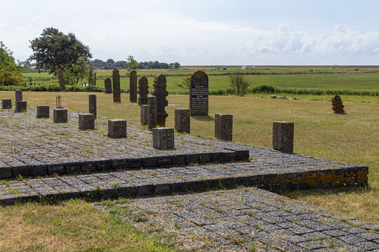 View of Strieperkerkhof with historic stone markers and a paved path set in a grassy field under a blue sky in Baaiduinen, Friesland, Netherlands.