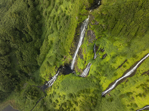Aerial view of Cascata da Ribeira do Ferreiro with multiple waterfalls cascading down a lush green cliffside covered in dense vegetation in Fajazinha, Azores, Portugal.