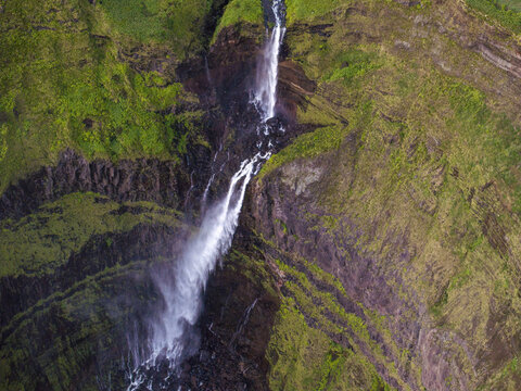 Aerial view of Cascata da Ribeira Grande cascading down lush green volcanic cliffs in the Azores. Faja Grande, Acores, Portugal.