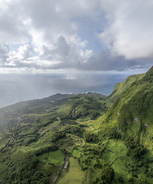 Aerial view of Cascata da Ribeira do Ferreiro with lush green cliffs, rolling hills, and agricultural fields overlooking the Atlantic Ocean in Fajazinha, Azores, Portugal.