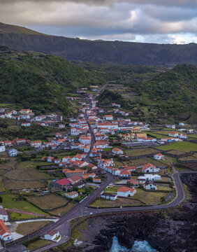 Aerial view of the village nestled in a lush green valley with stone walls, winding roads, and coastal cliffs in Faja Grande, Azores, Portugal.