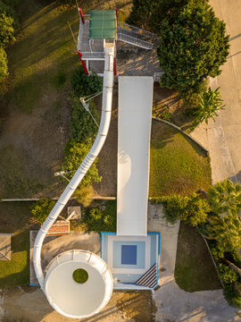 Aerial view of a white water slide with a bowl section and a straight chute surrounded by lush greenery and palm trees in Kos, Greece.