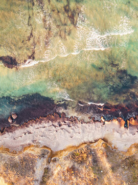Aerial view of the rugged coastline with turquoise sea water meeting rocky cliffs and sandy shores in Kos, Greece.