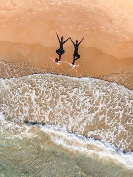 Aerial view of two people standing on a sandy beach with their shadows cast on the sand near the gentle waves of the sea in Kos, Greece.