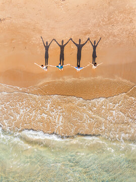 Aerial view of four people standing on a sandy beach with their shadows cast on the sand near the clear turquoise water in Kos, Greece.