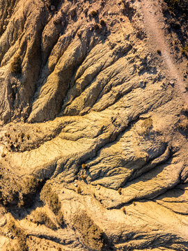 Aerial view of the rugged, eroded terrain featuring deep gullies, dry soil, and sparse vegetation under warm sunlight in Kos, Greece.