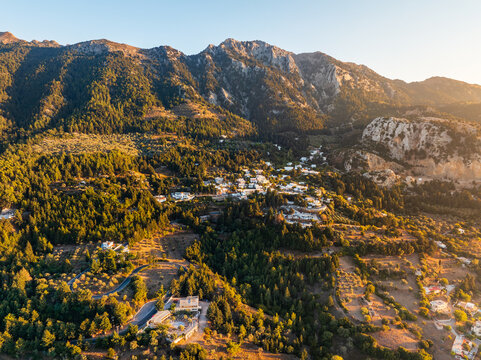 Aerial view of Zia village nestled in the mountainous landscape of Kos, surrounded by dense forests and winding roads under the warm glow of the golden hour, Kos, Greece.