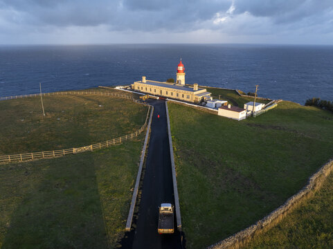 Aerial view of Farol de Alvernaz lighthouse situated on a grassy cliffside overlooking the Atlantic Ocean with a road leading to the structure in Ponta Delgada, Acores, Portugal.