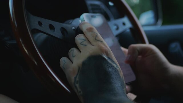 Close-up of tattooed hands using a smartphone inside a car, representing modern technology, mobile connectivity, digital communication, and everyday innovation.